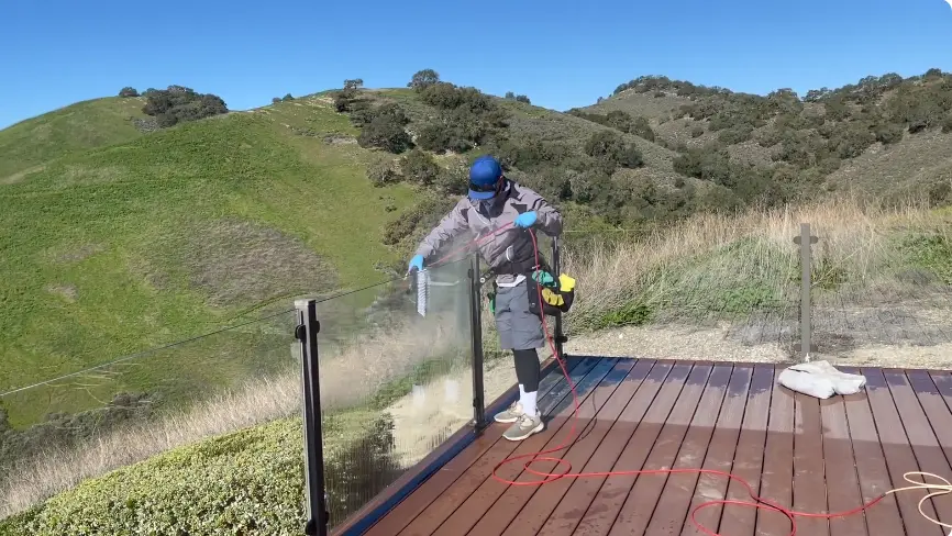 Cleaning a Glass Deck Railing Technician cleaning a glass railing on a wooden deck with a hillside view