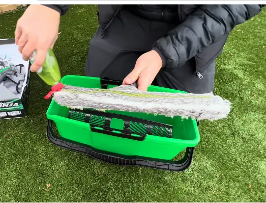 Window cleaner spraying cleaning solution onto a strip washer over a green bucket