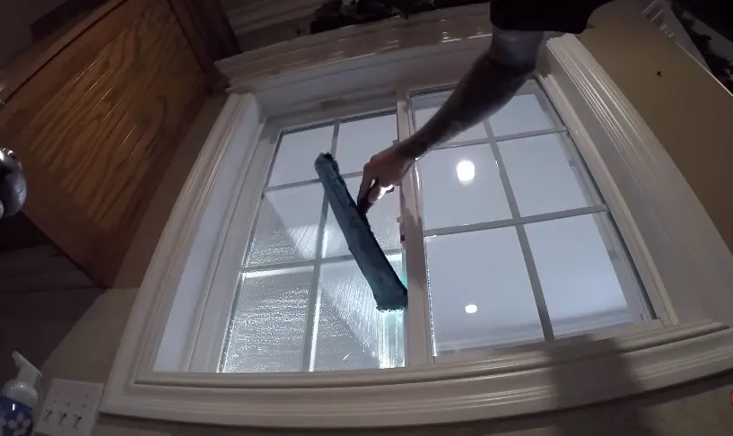 Squeegee clearing the inside of a divided-light window with a white wood frame