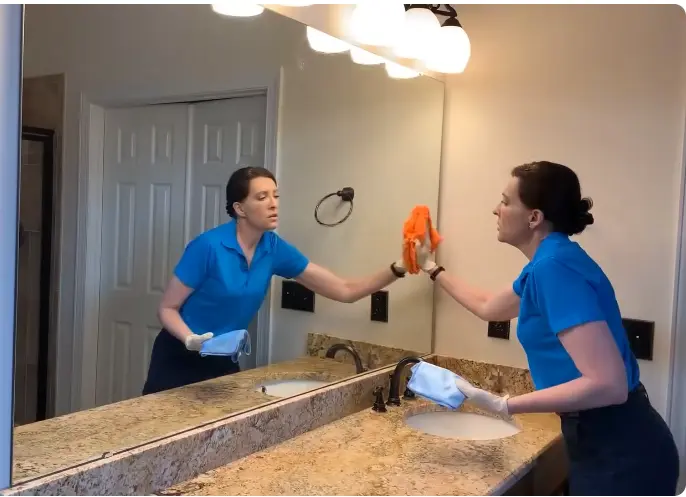 Cleaning a Large Bathroom Mirror Cleaner in a blue uniform wiping a large bathroom mirror above a vanity