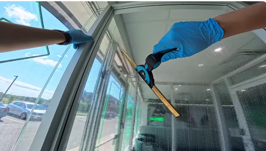 Gloved hand pulling a squeegee down the inside of a large glass panel