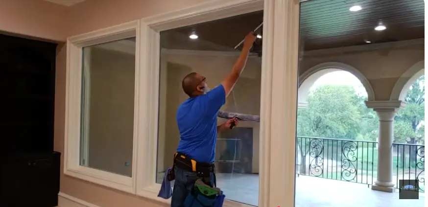 Interior window cleaning: technician using an extension pole on tall inside windows in a bright room with arched glass
