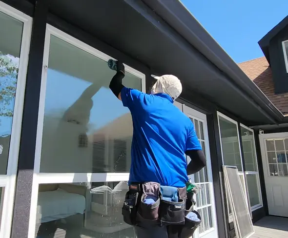 Cleaning Outside Glass Panels Window cleaner in a blue jacket cleaning tall outside glass panels under a roof overhang