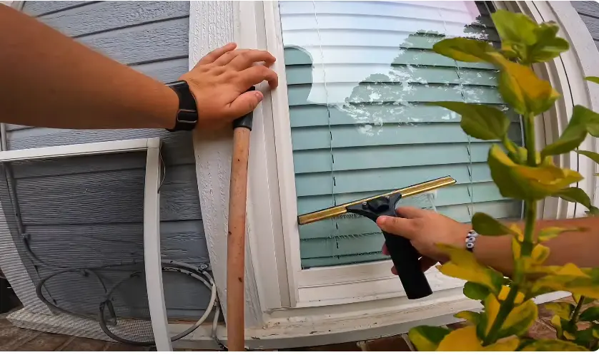 Wiping an Exterior Window Frame Technician wiping the frame of an exterior window beside siding and shrubs