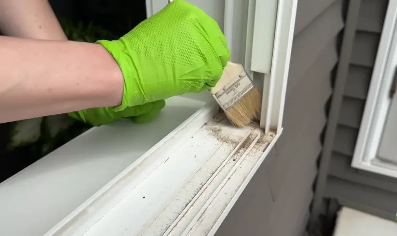Dry-Brushing a Window Track Gloved hand dry-brushing dirt out of a window track with a small paintbrush